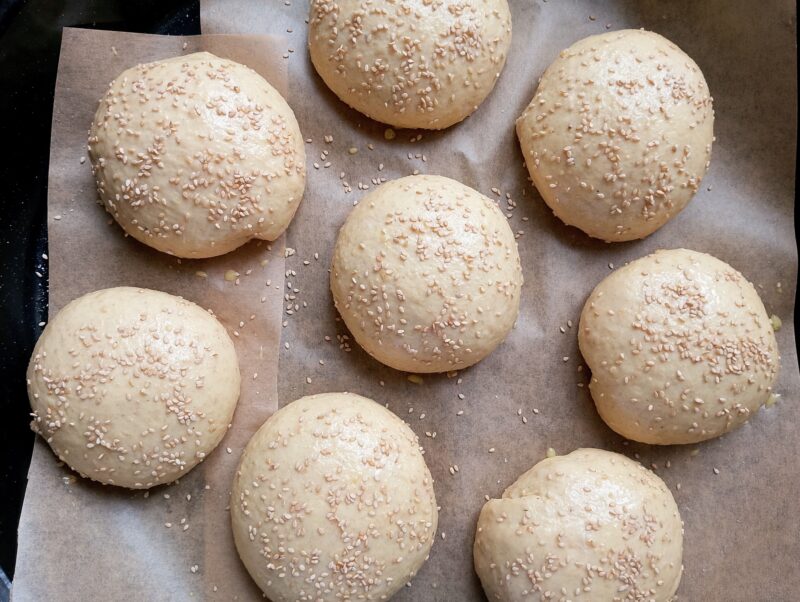 Unbaked sourdough discard burger buns, glazed with egg wash and sprinkled with sesame seeds