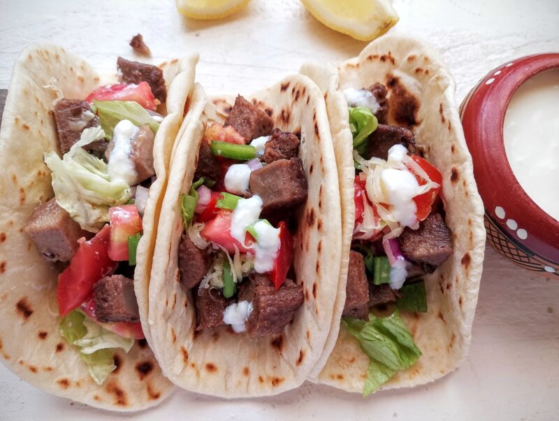 Beef tongue tacos on table, with a bowl of sour cream on the side