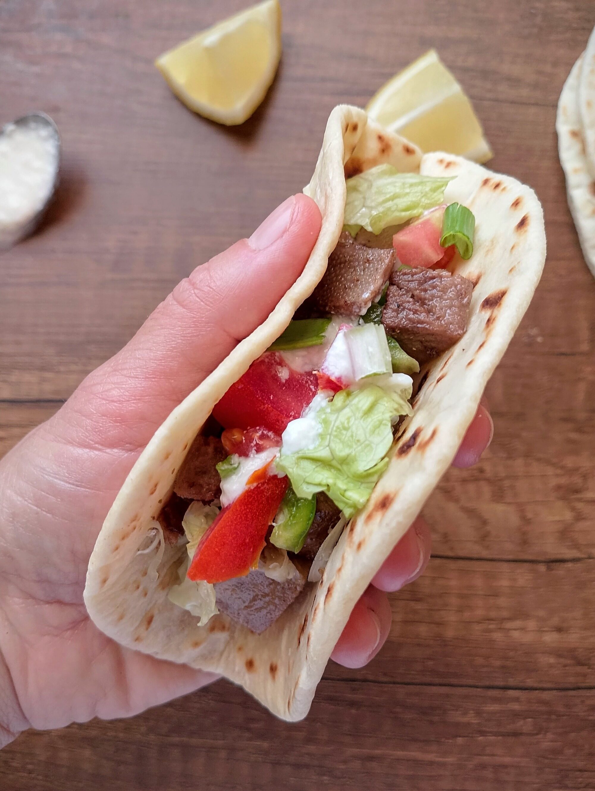 Hand holding beef tongue taco with salsa, lettuce, and sour cream