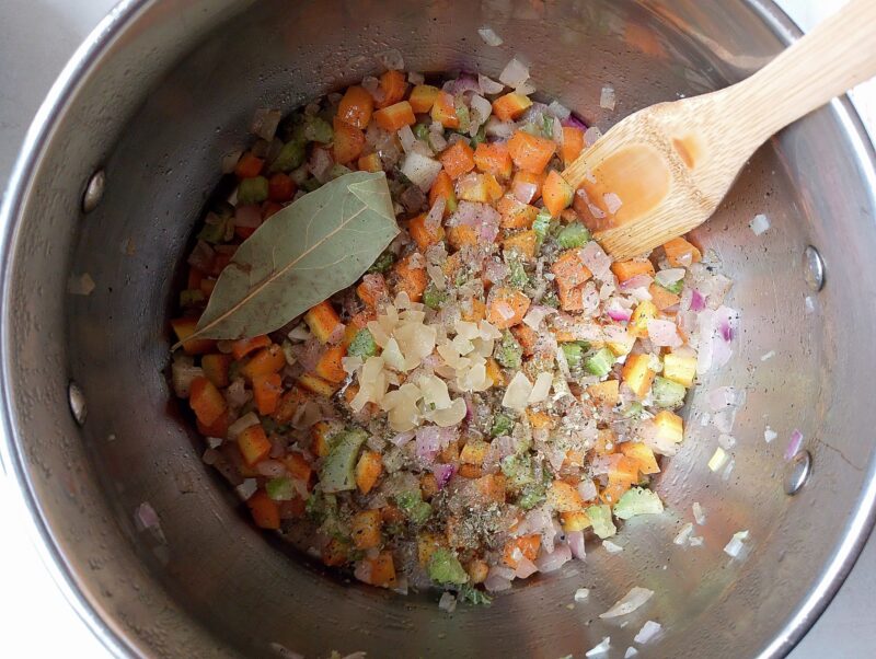 Adding garlic, bay leaf, and marjoram to the pot with sauteed vegetables