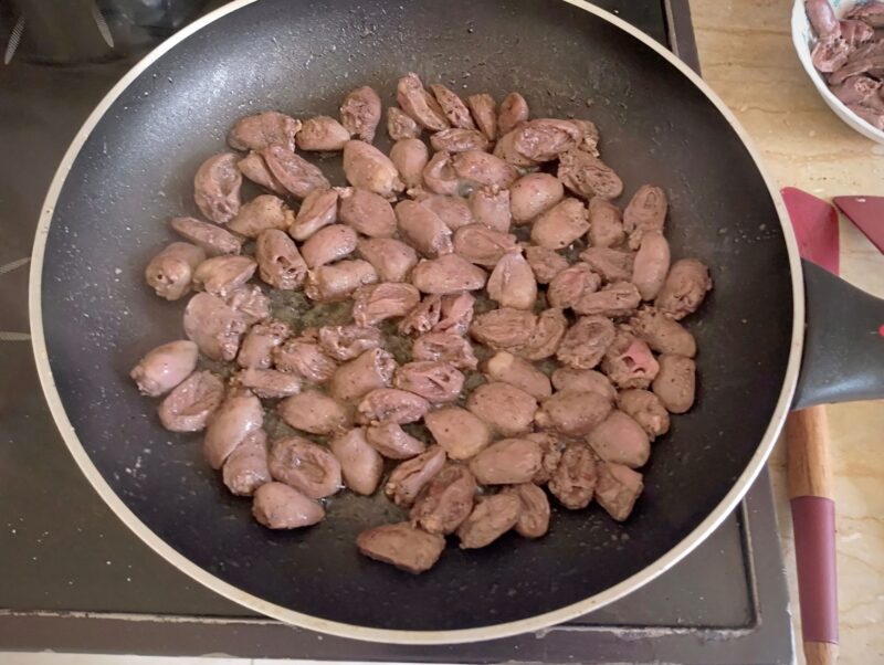 Cooking halved chicken hearts in a skillet
