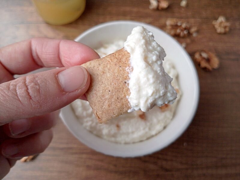 Hand lifting a cracker dipped in homemade fromage blanc