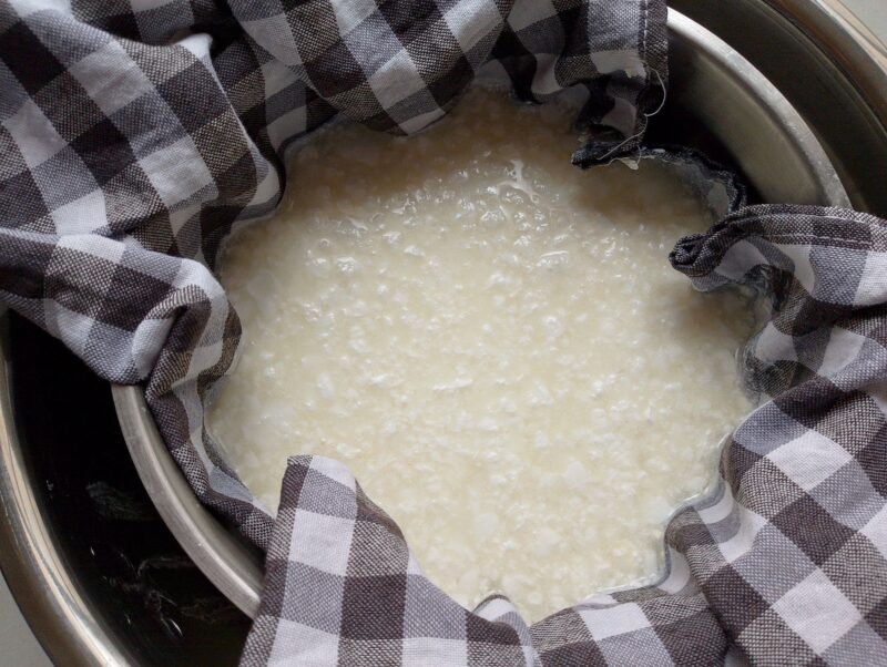 Curds draining in a colander lined with cheesecloth