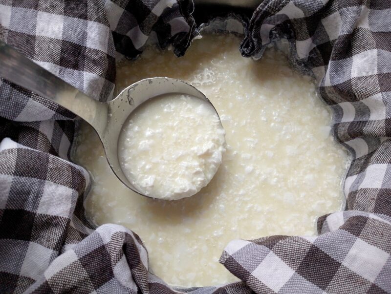 Ladle transferring curds into a colander lined with cheesecloth