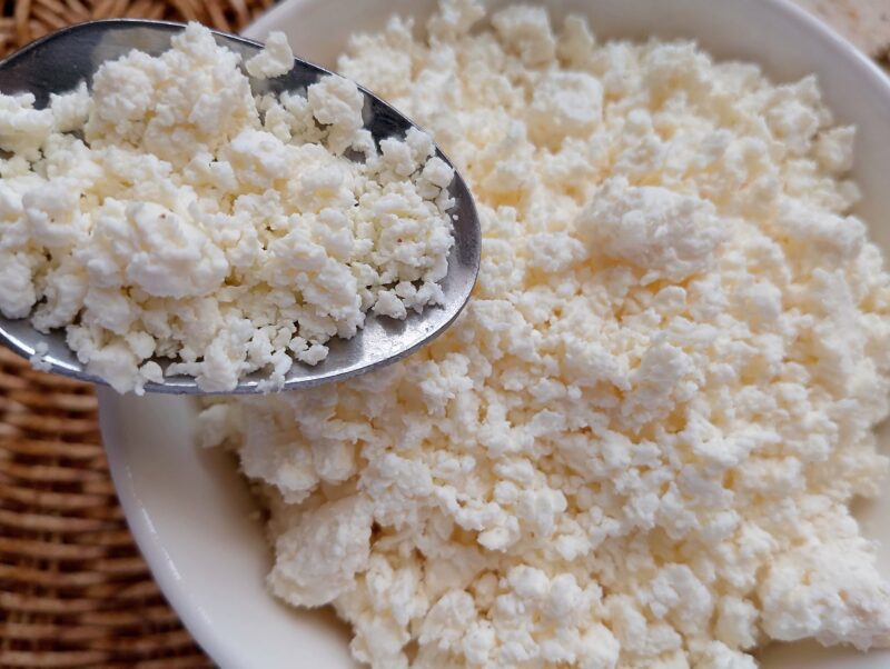 Spoon lifting raw milk farmer's cheese out of a bowl