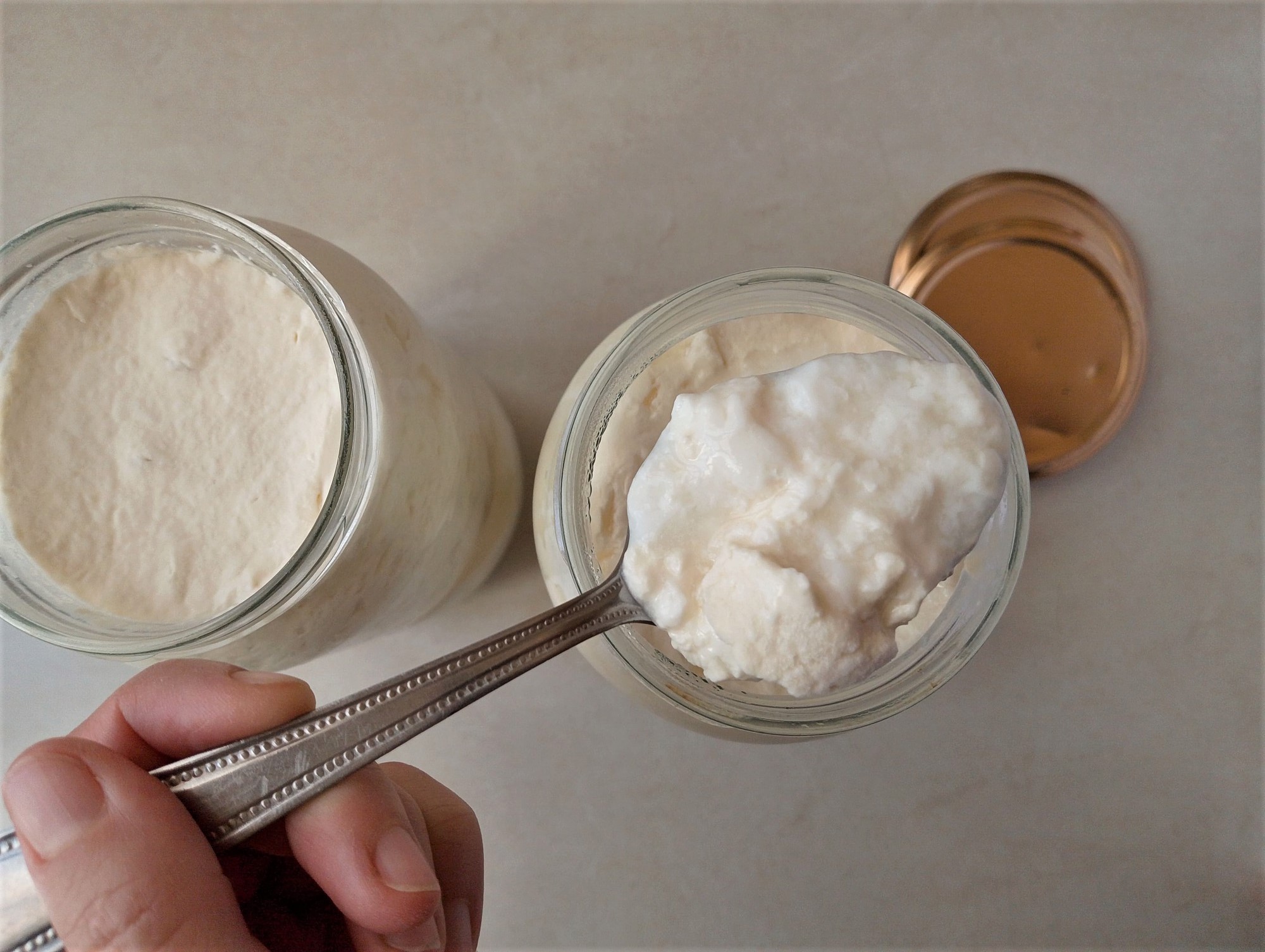 Hand lifting a spoon with some clabbered milk out of a jar