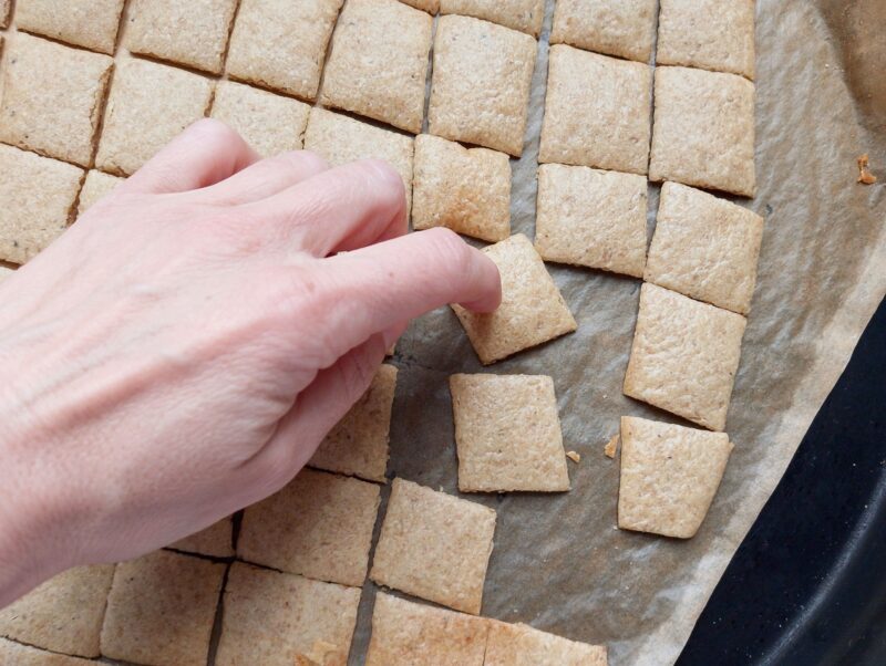 Woman tapping a sourdough cracker with fingernail to check for doneness