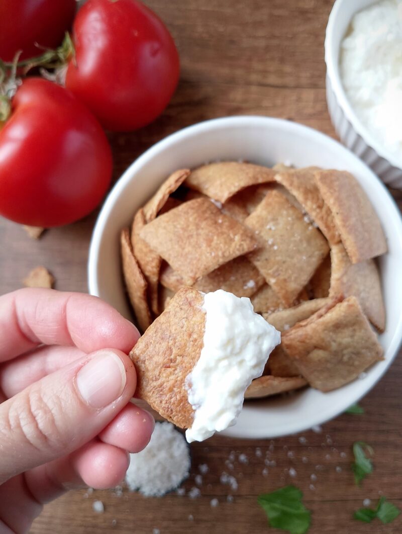 Hand lifting a whole wheat sourdough cracker dipped in cottage cheese