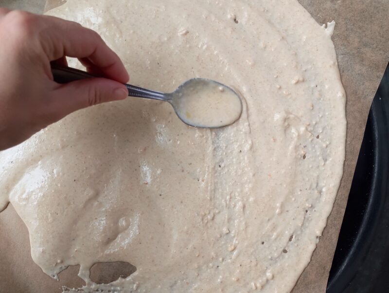 Spreading the batter for sourdough crackers recipe on a baking sheet lined with parchment