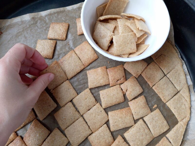 Woman transferring freshly baked sourdough crackers to a serving bowl