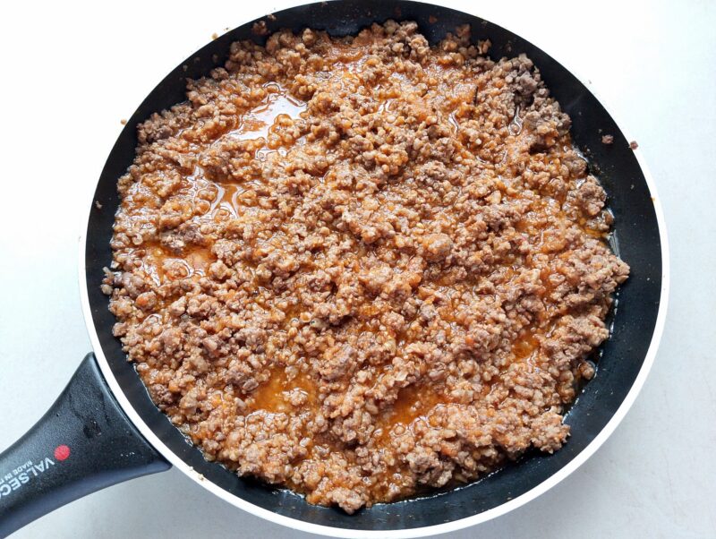 Adding tomato sauce and seasonings to ground meat in skillet