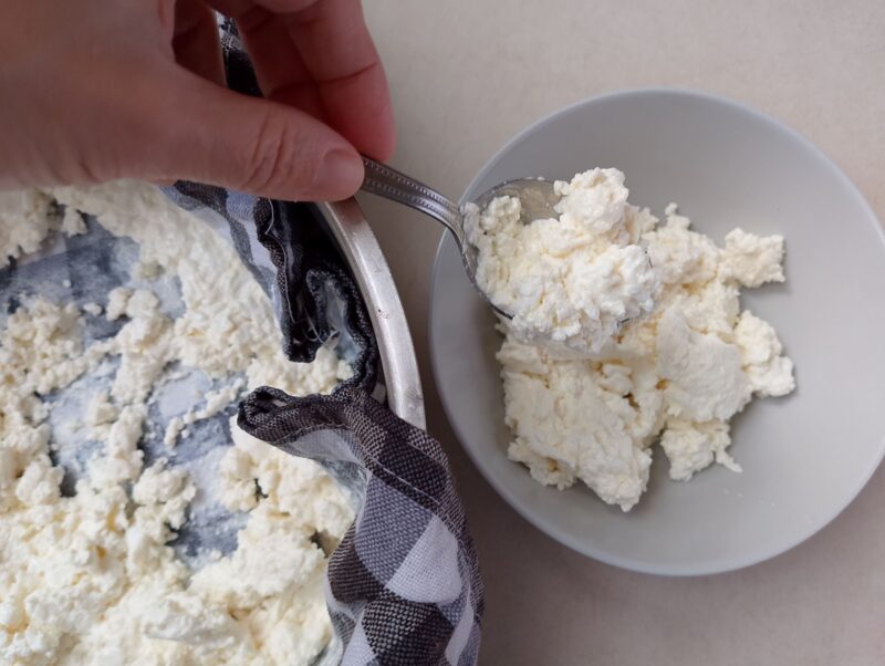 Hand spooning well drained whey ricotta from cheesecloth to serving bowl
