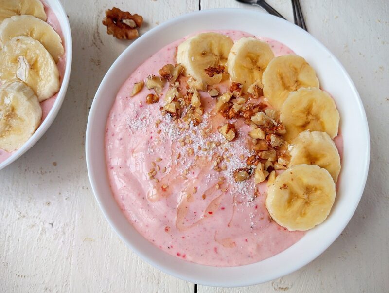 Healthy strawberry and banana smoothie bowl topped with sliced bananas, nuts, seeds, and shredded coconut