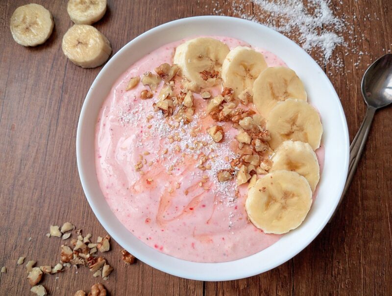 Healthy smoothie bowl with cottage cheese and kefir, topped with sliced bananas and chopped nuts