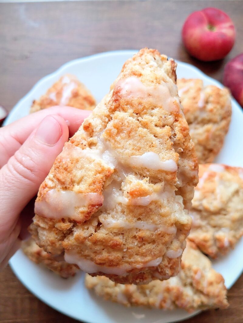 Hand holding freshly baked sourdough discard scone with glaze drizzled on top