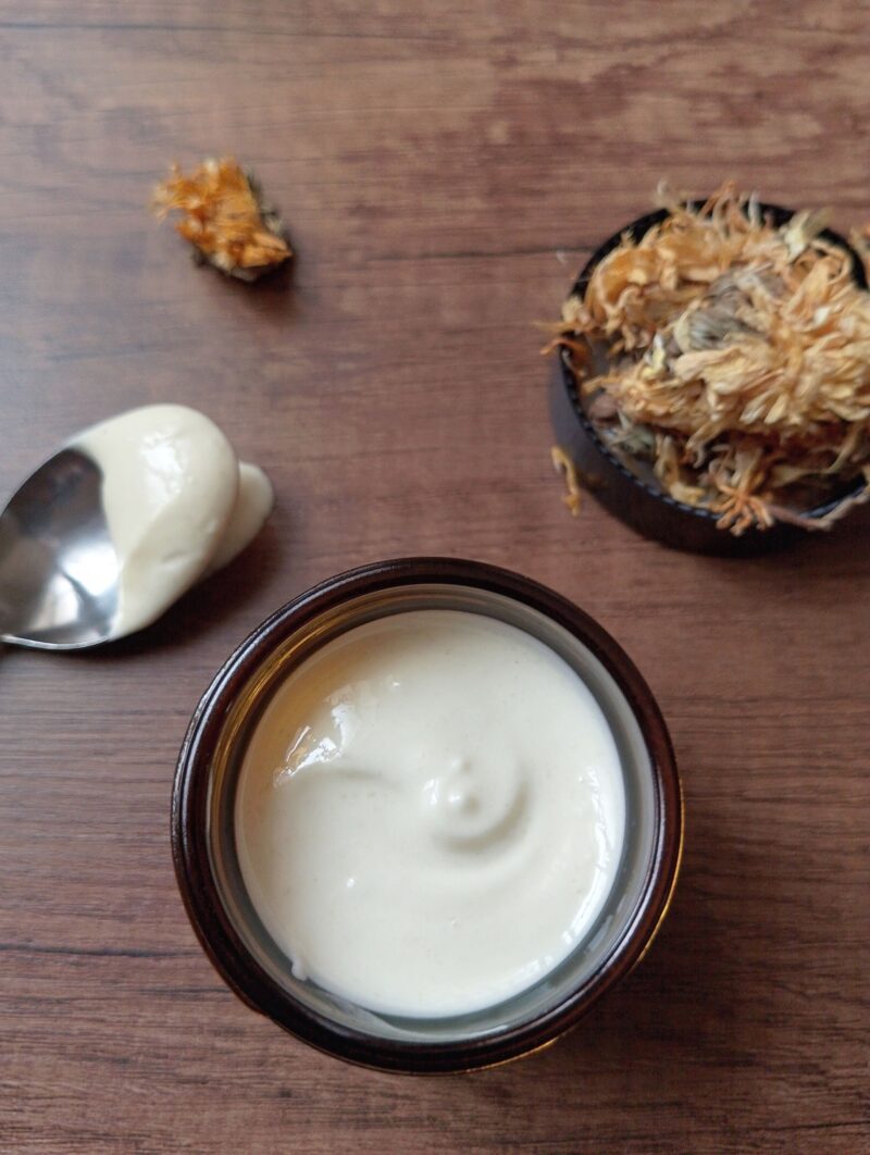 Calendula tallow body cream in amber glass jar with a spoon scooped out on the side