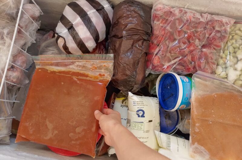 Woman's hand reaching for a ziplock bag of tomato sauce in chest freezer