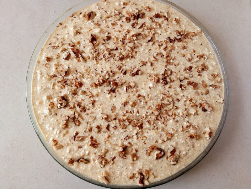 Sprinkling chopped walnuts over unbaked breakfast bake in baking dish