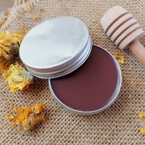 Homemade tallow lip balm in metal tin, with dried calendula flowers scattered around