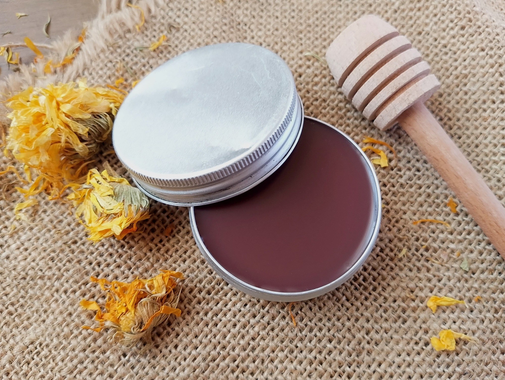 Homemade tallow lip balm in metal tin, with dried calendula flowers scattered around