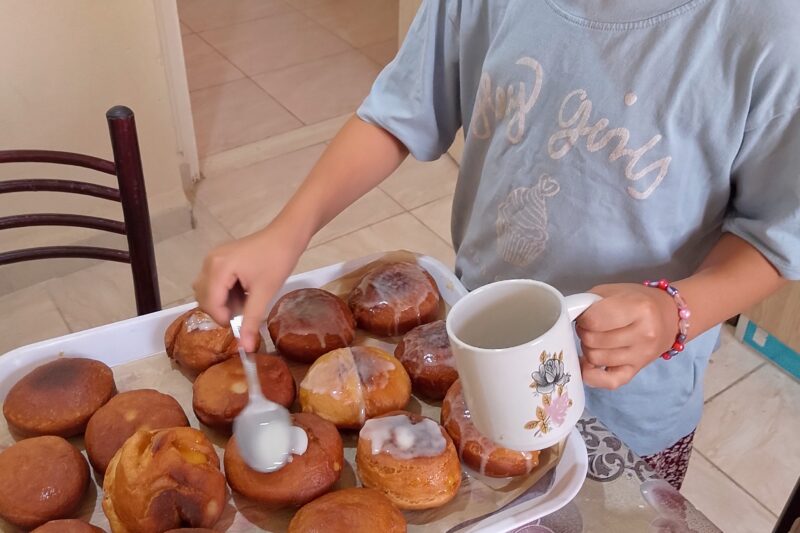 Child glazing donuts on tray