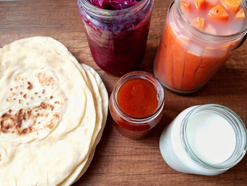 Homemade tortillas, sauerkraut, fermented carrots, jam, and homemade yogurt on wooden table
