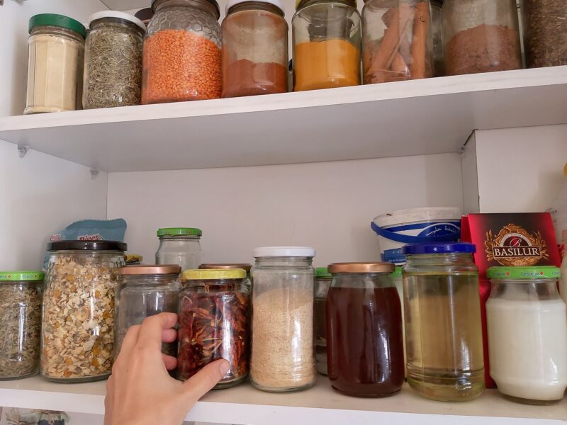 Spice and dry ingedient cabinet full of jars with hand reaching for a jar