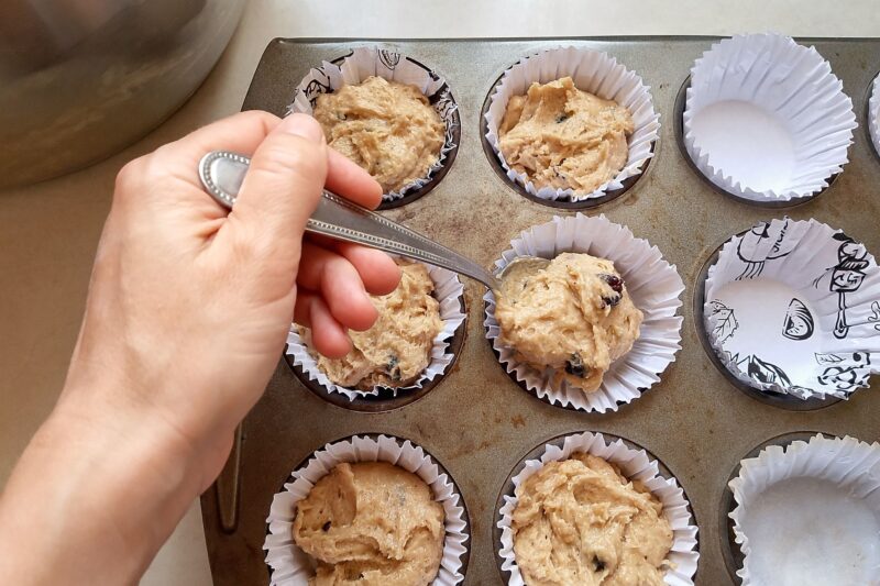 Womans hand with spoon filling muffin liners with muffin batter