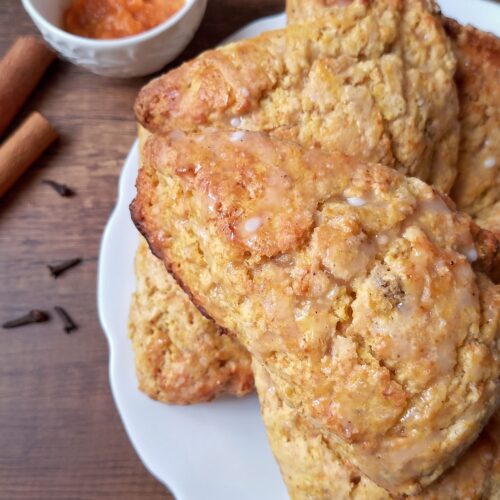 Sourdough pumpkin scones on white serving plate with cinnamon and bowl of pumpkin puree on the side