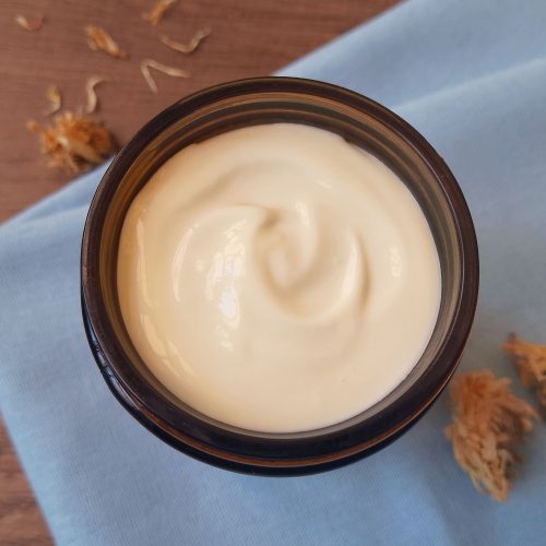 Calendula body butter in amber glass jar on blue napkin