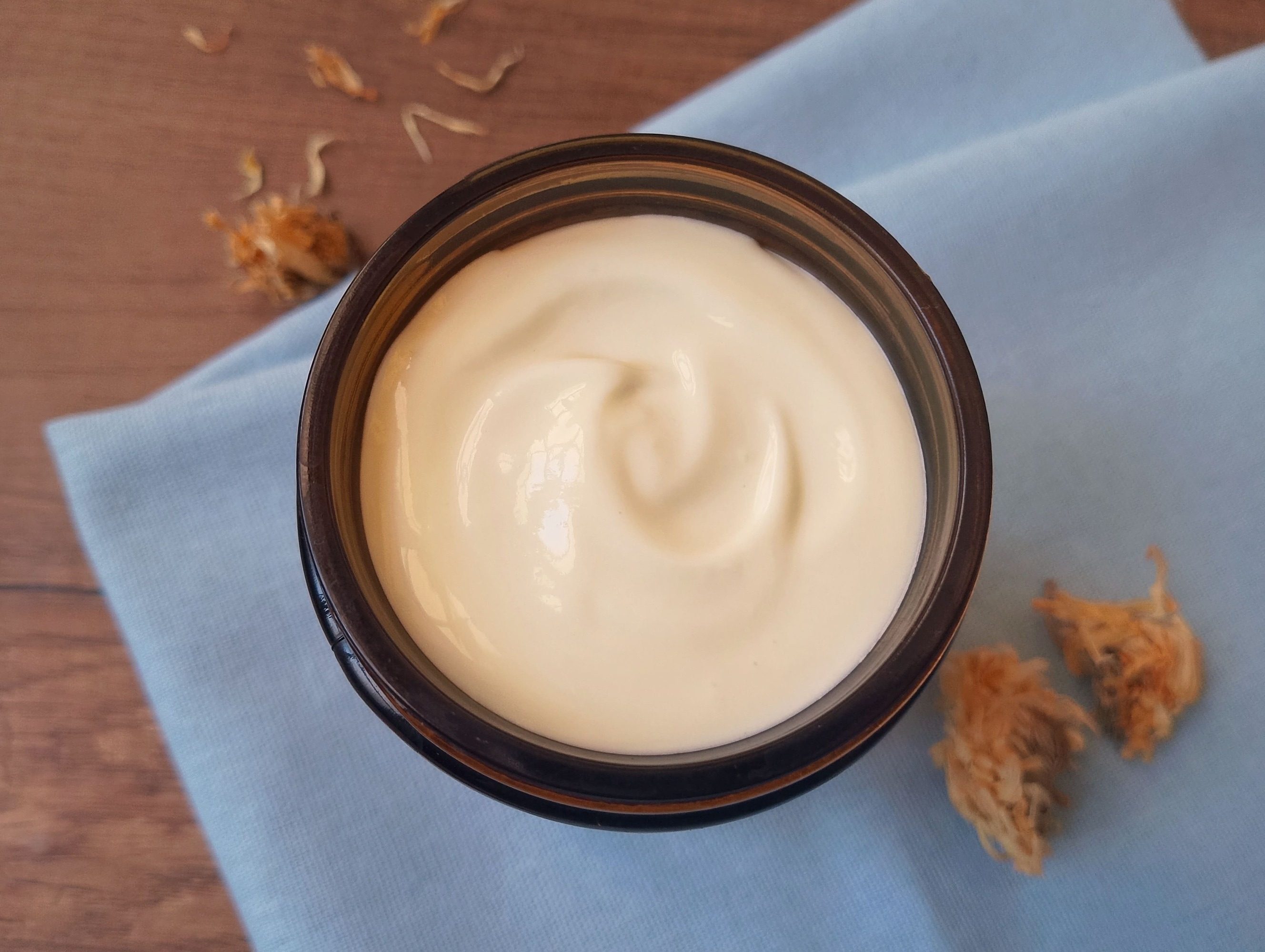 Calendula body butter in amber glass jar on blue napkin