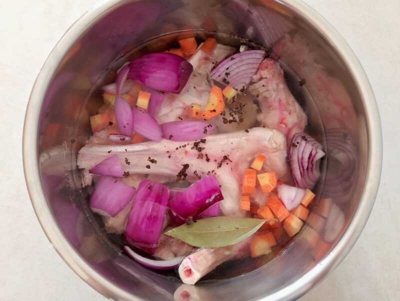 Lamb bones and vegetables covered with water in pot