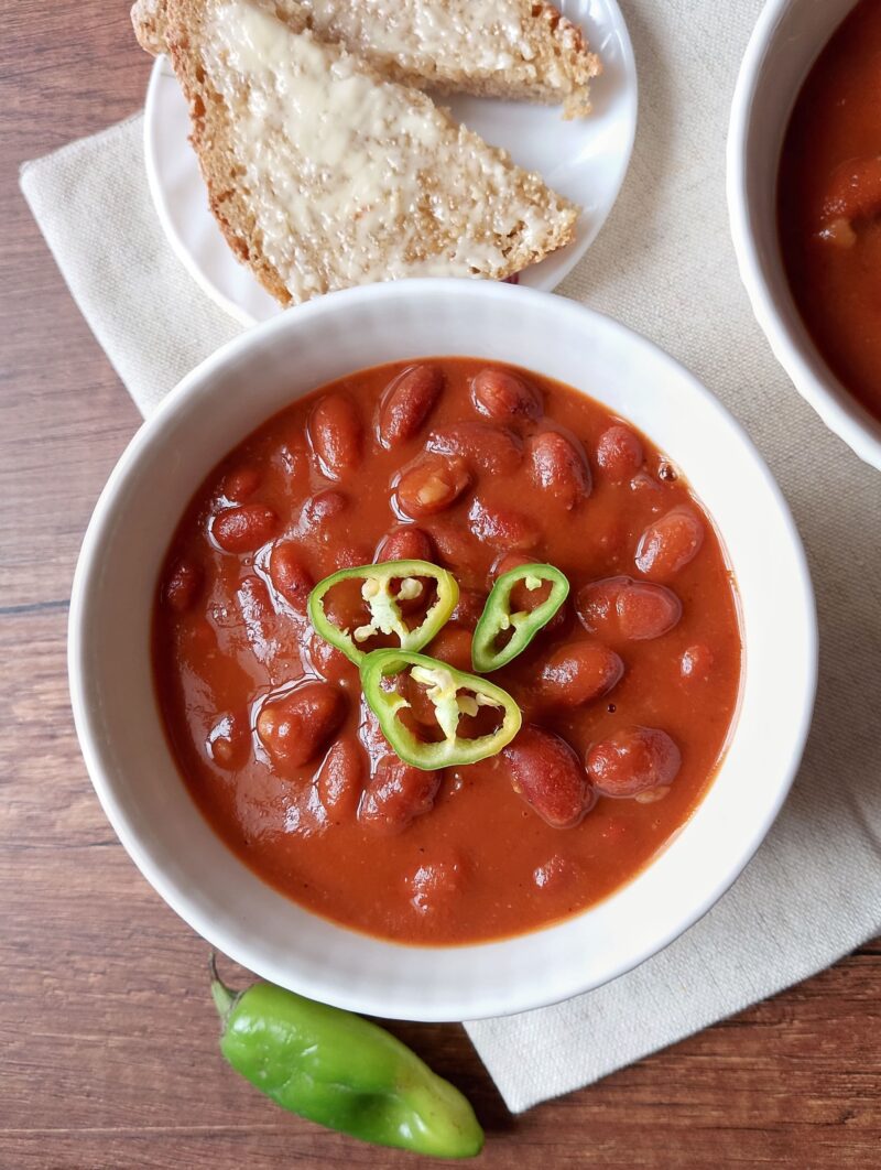 Baked beans in bowl garnished with sliced green chilies and served with buttered bread