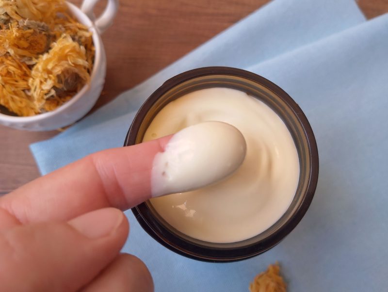 Finger scooping some calendula body butter out of jar