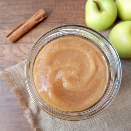 Instant Pot applesauce in jar on burlap with cinnamon stick and apples in background