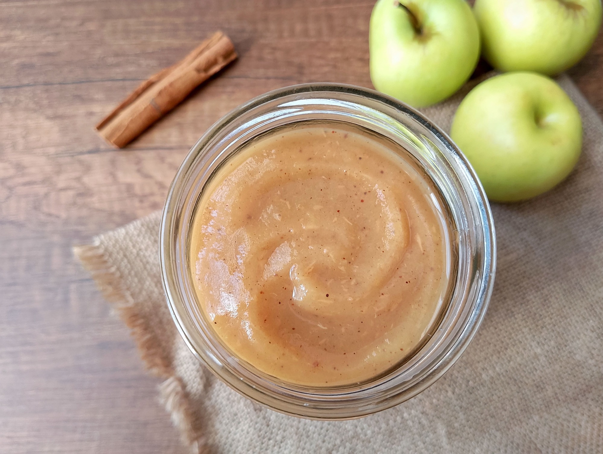 Instant Pot applesauce in jar on burlap with cinnamon stick and apples in background
