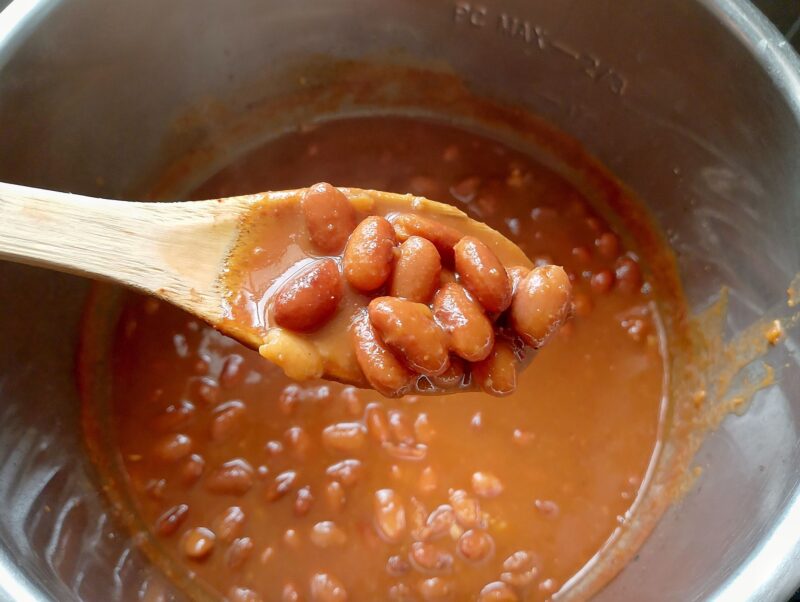 Wooden spoon lifting some baked beans out of instant pot