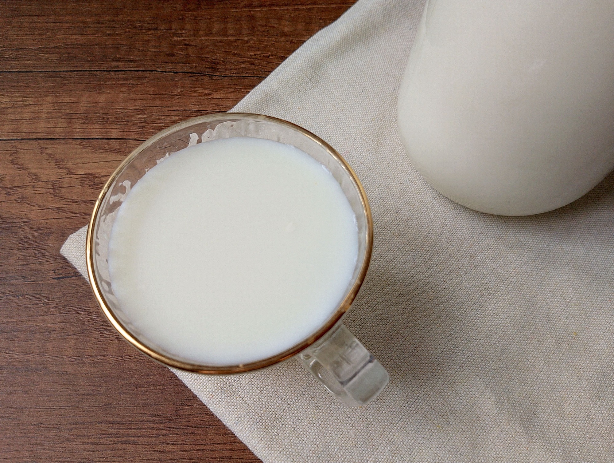 Raw milk benefits: glass of raw milk on table with jar of raw milk beside it