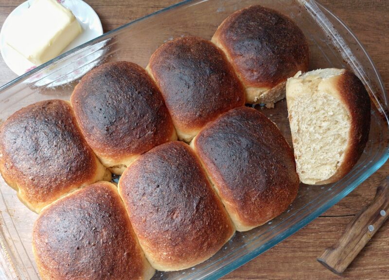 Freshly baked soft sourdough rolls in pan with one roll facing up so the crumb is visible